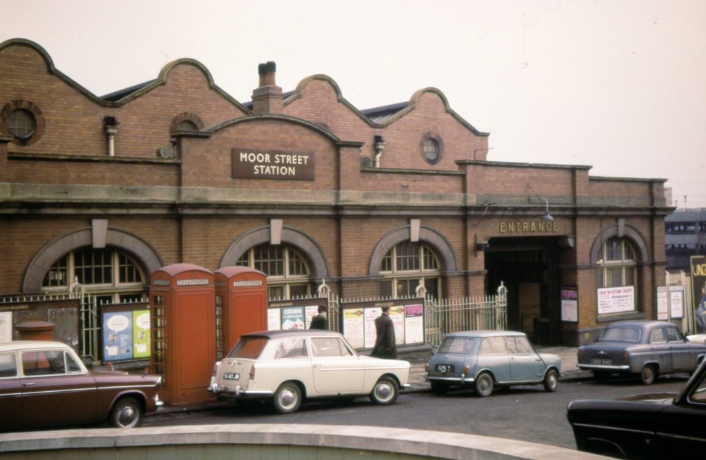 1963年のムーア・ストリート駅。赤レンガの駅舎とクラシックカーが並ぶ英国バーミンガムの街角。