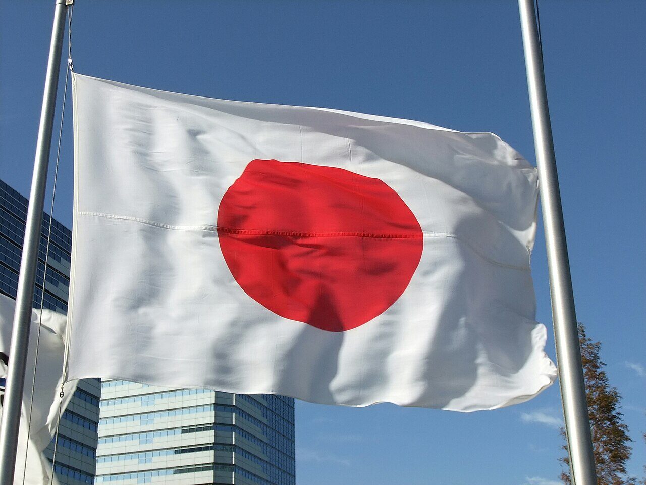青空に掲げられた日本国旗（日の丸）。白地に赤い円が描かれた、太陽を象徴する国家のシンボル。