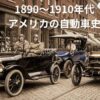 1910年代のアメリカの街並み。フォード・モデルT（ガソリン車）、デトロイト・エレクトリック（電気自動車）、スタンレー・スチーマー（蒸気自動車）が、それぞれのドライバーや乗客と共に混雑した石畳の通りに並んでいる様子。