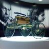 博物館に展示されたベンツ・パテント・モトールヴァーゲンとその開発者の肖像