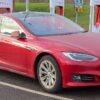 赤いテスラ・モデルSが専用充電ステーションで充電中。背景にはTeslaの急速充電設備が並ぶ。